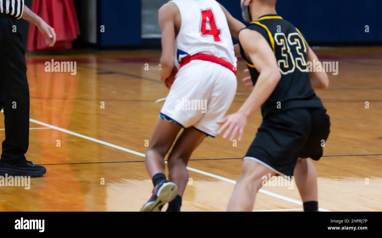 Il giocatore di basket è sorvegliato dal difensore mentre il giocatore ufficiale guarda durante una partita di scuola superiore. Foto Stock