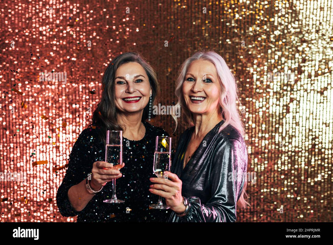 Le donne anziane di stile si ergono insieme sullo sfondo glitterato che tiene i bicchieri di champagne Foto Stock