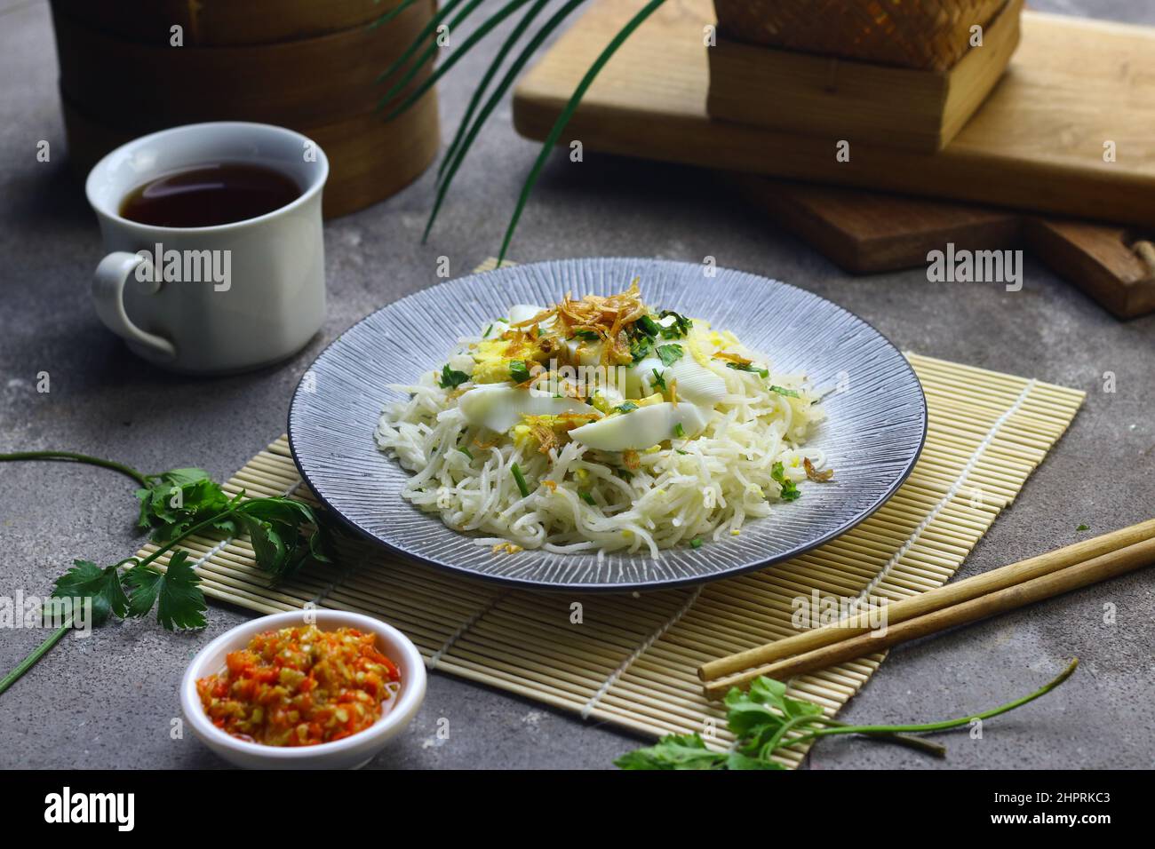 Bihun Goreng o spaghetti di riso fritti serviti su piastra di ceramica, conditi con fette di uovo bollito con sambal. Sfondo grigio granulato. Foto Stock