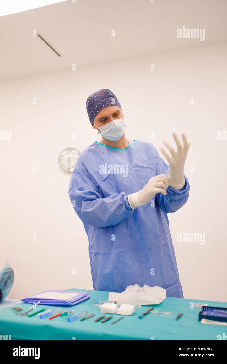 Chirurgo maschio che mette i suoi guanti sterili e si prepara per un intervento chirurgico Foto Stock