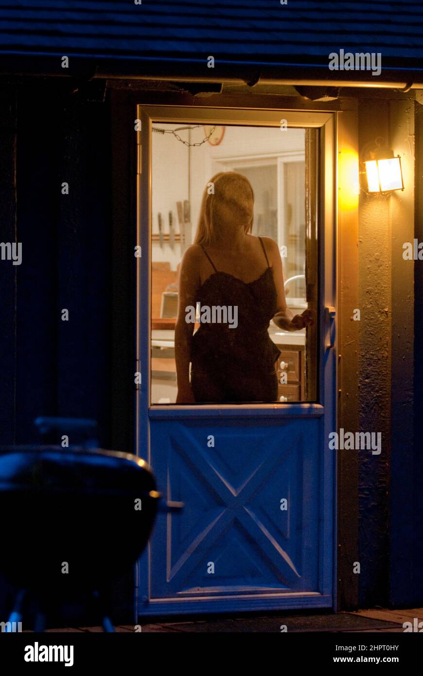 Giovane donna in piedi alla porta dello schermo, guardando fuori Foto Stock