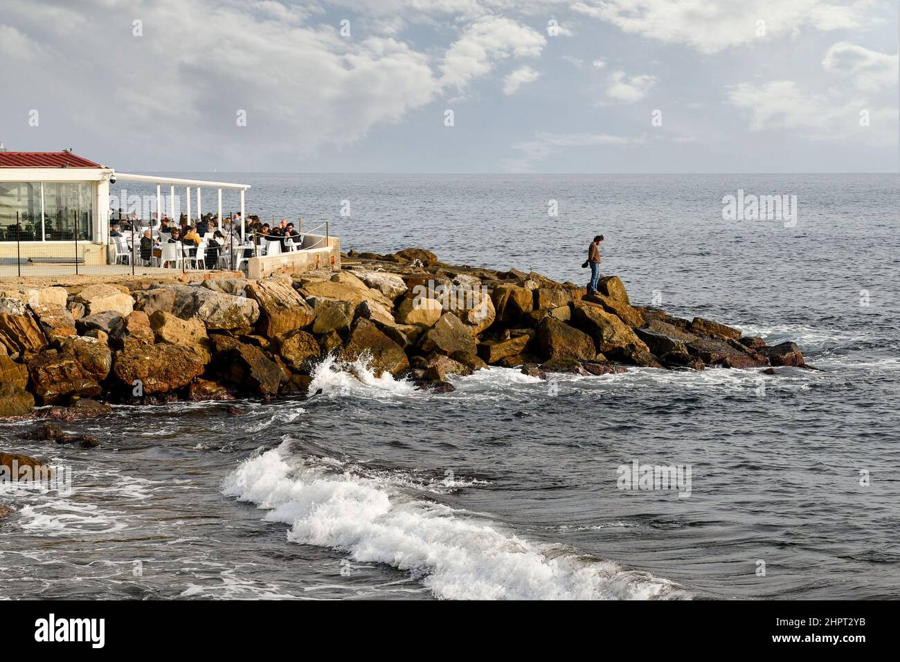 Stagcape con persone che pranzano in un ristorante sulla spiaggia sulla costa rocciosa in una giornata invernale, Sanremo, Imperia, Liguria, Italia Foto Stock