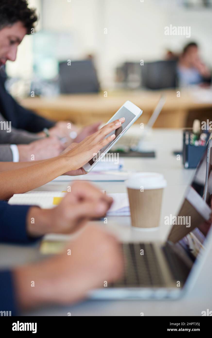 Questa azienda è all'avanguardia. Scatto ritagliato di un gruppo di professionisti aziendali seduti intorno al tavolo in una riunione utilizzando la tecnologia moderna. Foto Stock