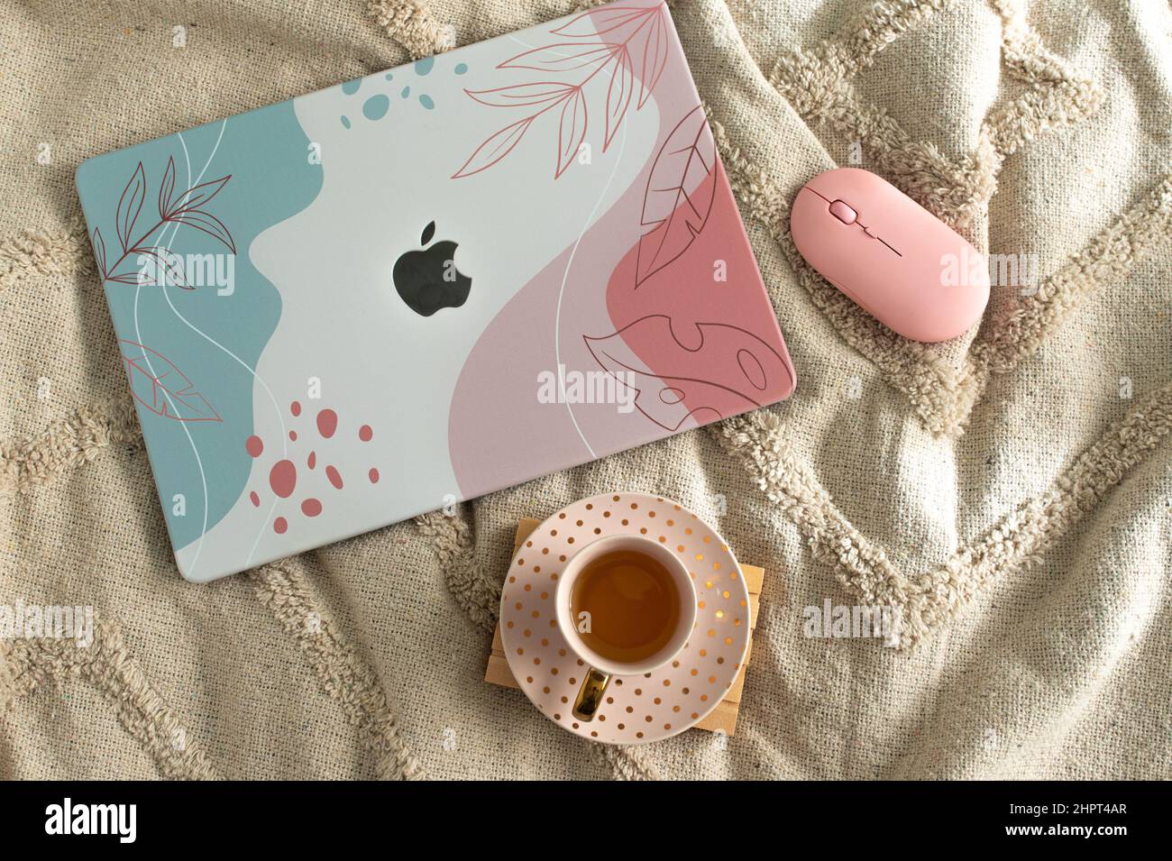 Computer portatile Macintosh con copertura colorata su un letto accanto a un mouse e una tazza di tè. Lavorare a casa. Foto Stock