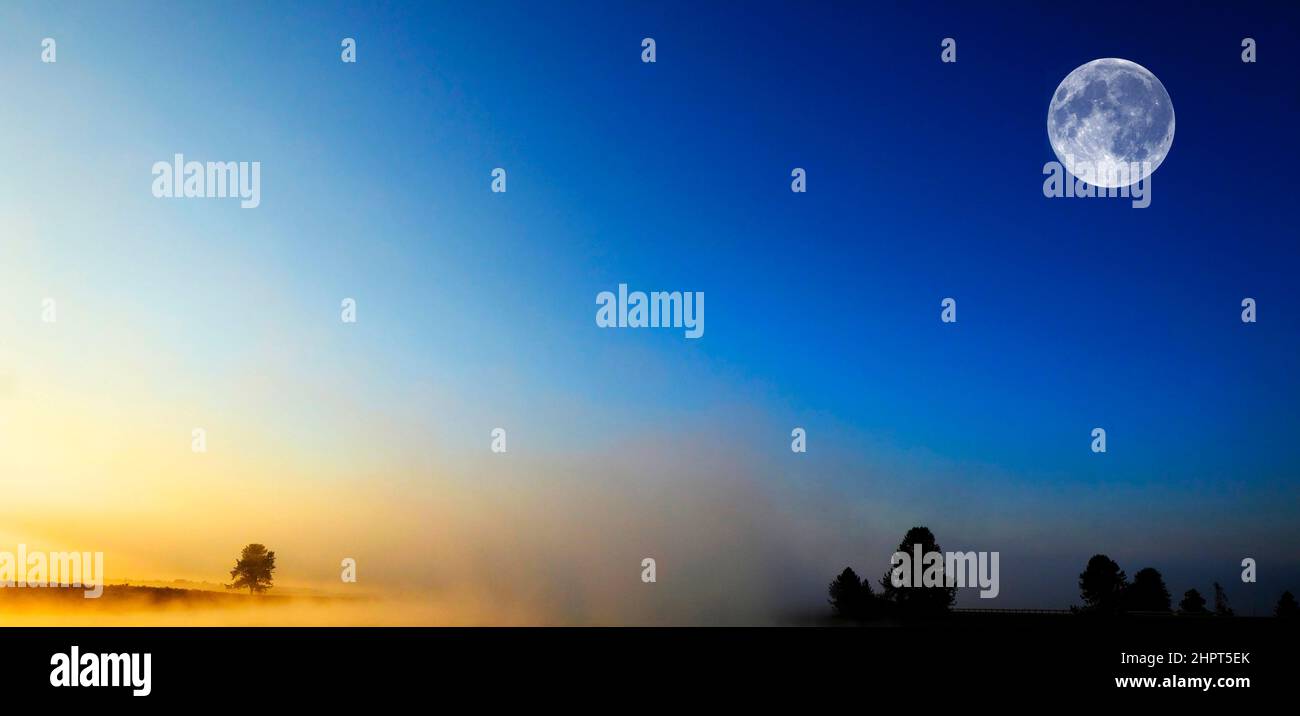 Alba del mattino con alberi e fiume sotto il cielo blu e la nebbia incandescente e luna piena Foto Stock