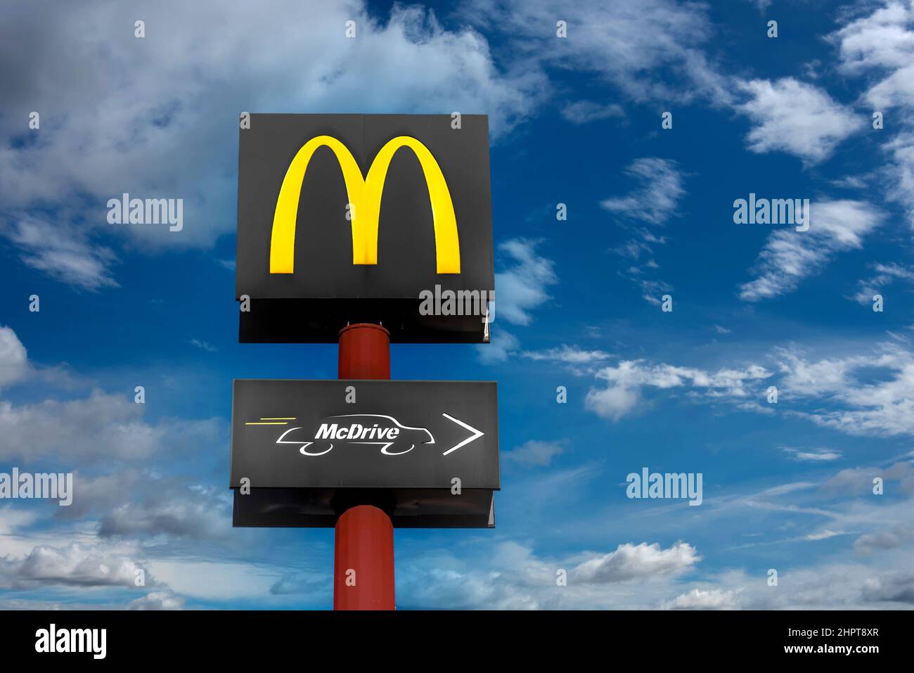 Fossano, Italia - 22 febbraio 2022: Cartello con il logo McDonald's Restaurant e cartello con il logo McDrive su palo rosso su cielo blu con nuvole. È il lar del mondo Foto Stock