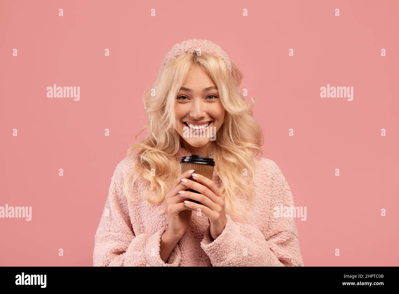 Bevanda calda e pausa preferite. Signora felice che tiene takeaway tazza di carta e sorridente alla macchina fotografica, in piedi su sfondo rosa Foto Stock