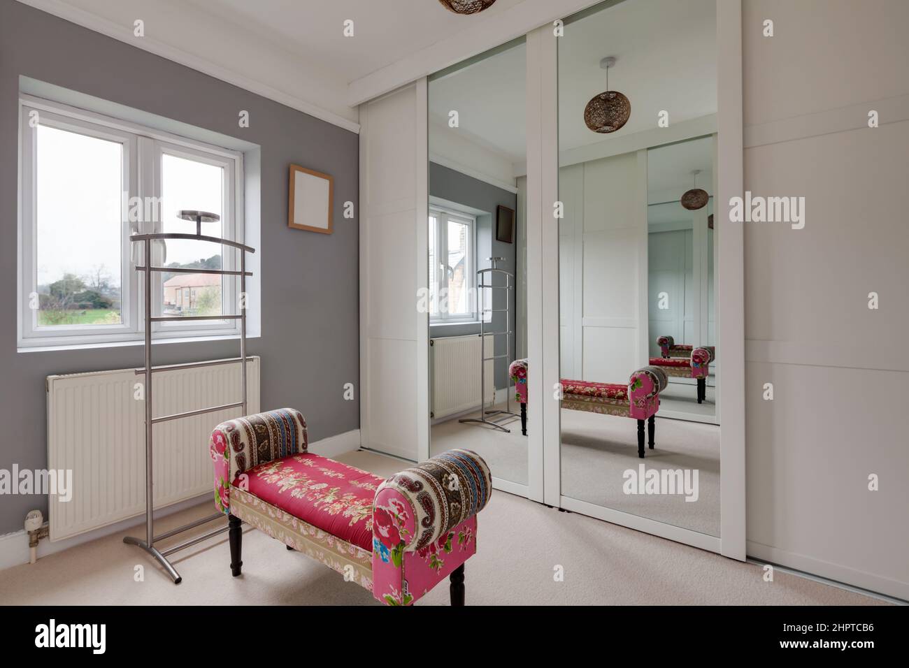 Lo spogliatoio si riflette in una grande porta a specchio che dà l'impressione di uno spazio più grande con interessante sgabello rosa e decorato in grigio e bianco Foto Stock