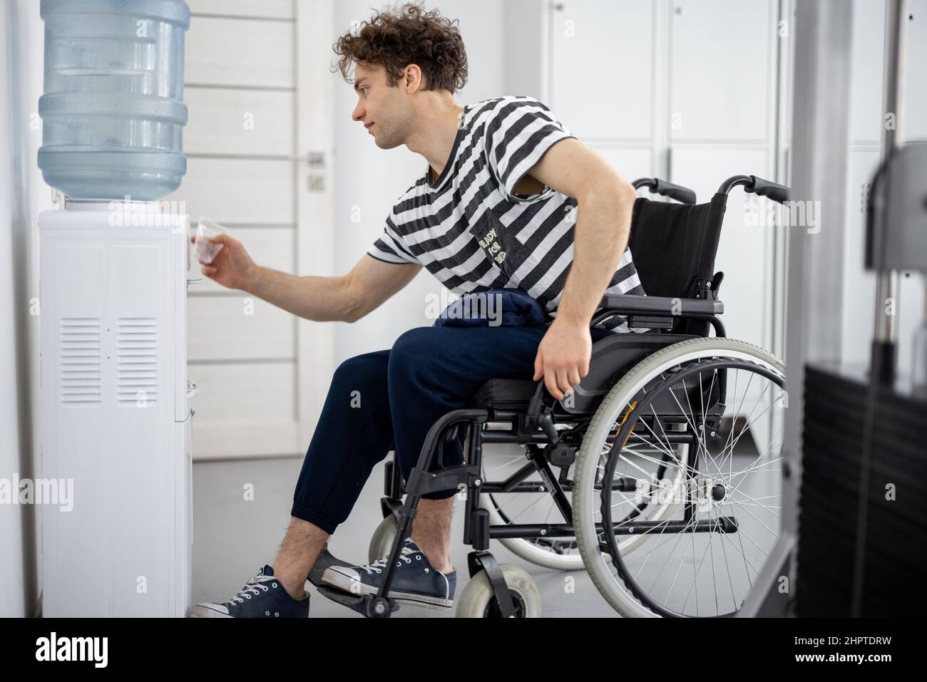 Ragazzo su una sedia a rotelle cercando di ottenere l'acqua per bere da un refrigeratore Foto Stock