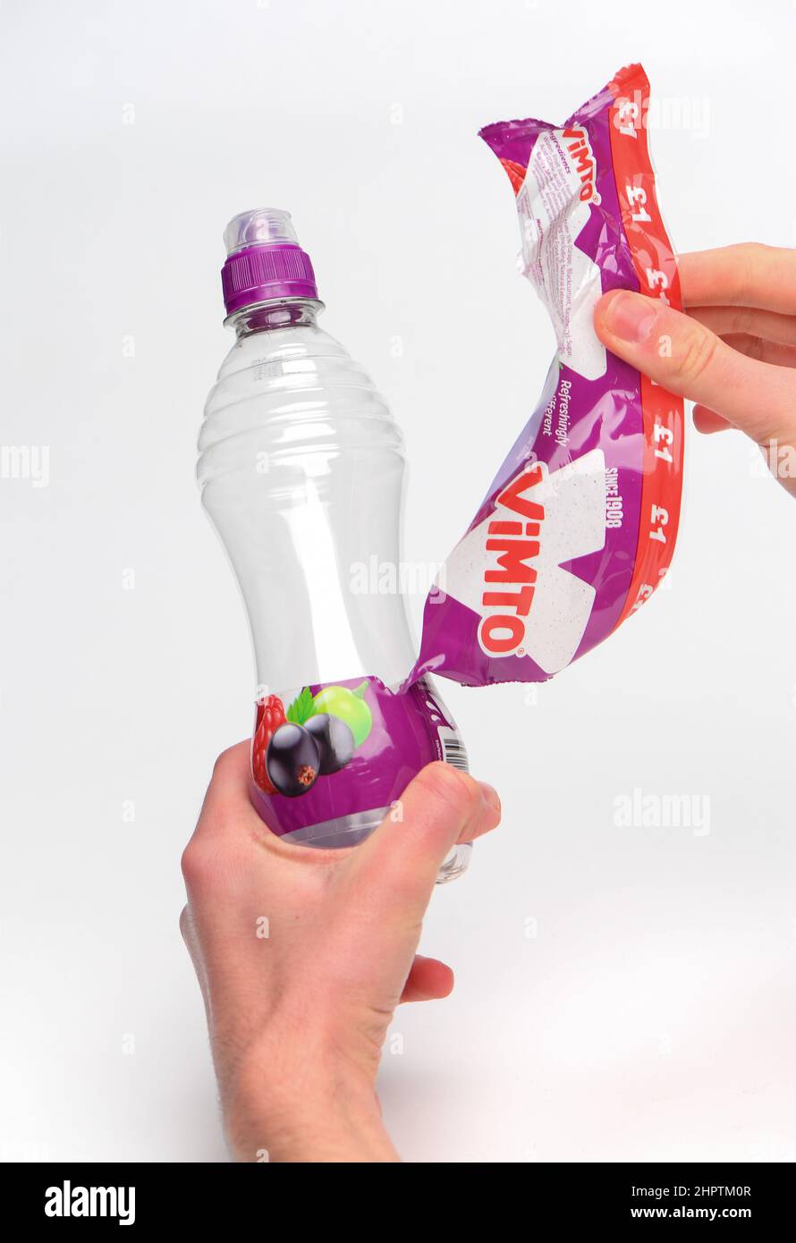 Rimozione dell'etichetta per il riciclaggio su una bottiglia di plastica Vimto monouso fotografata su sfondo bianco. Foto Stock