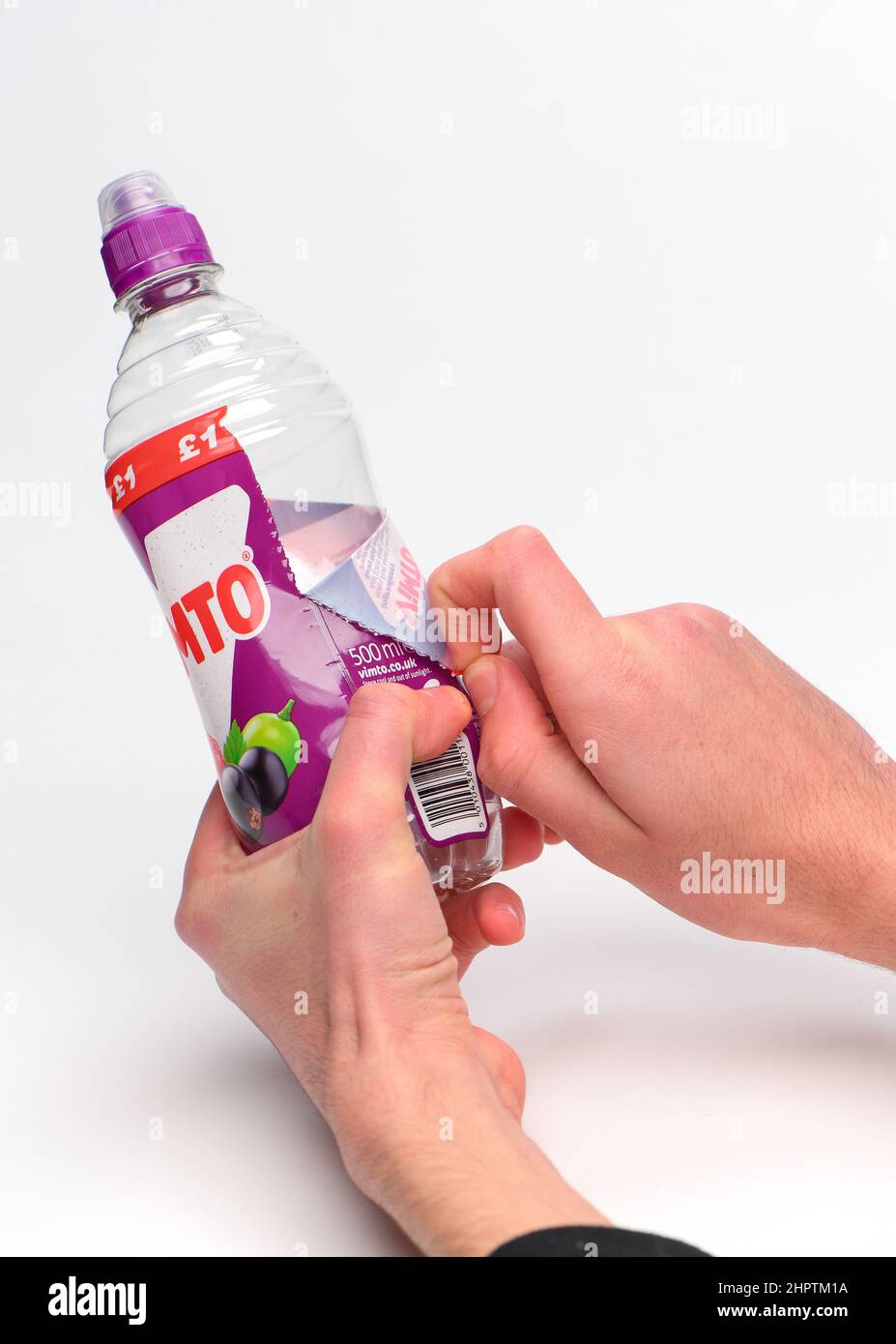Rimozione dell'etichetta per il riciclaggio su una bottiglia di plastica Vimto monouso fotografata su sfondo bianco. Foto Stock
