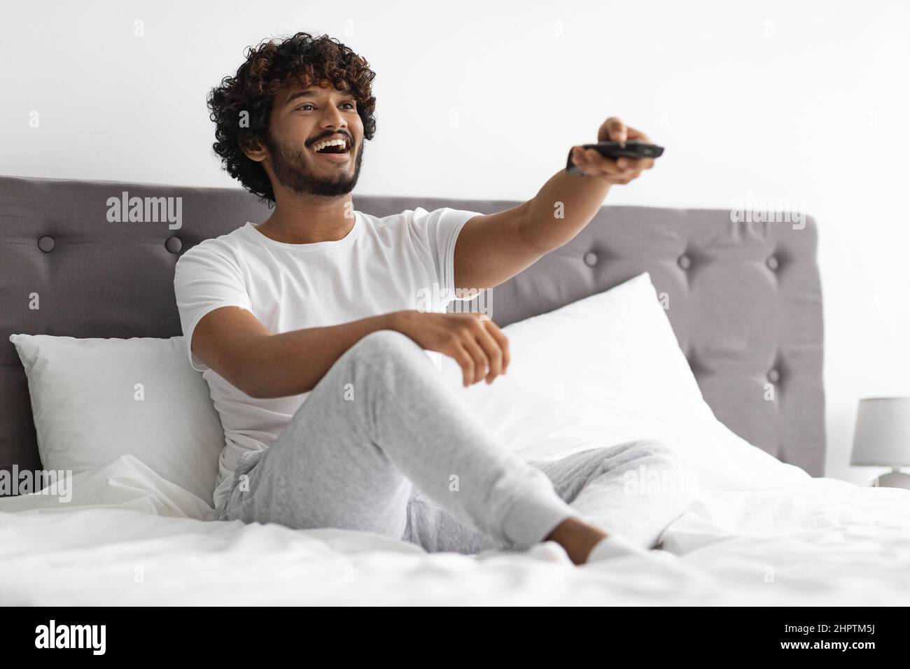Ragazzo hindu gioioso seduto a letto, guardando la TV Foto Stock