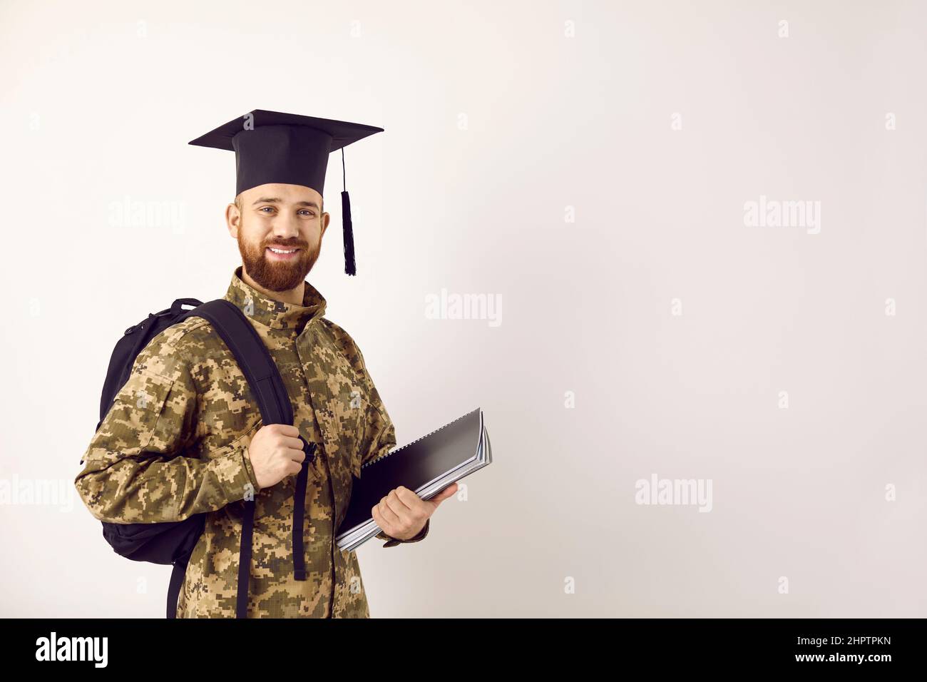 Felice studente militare in uniforme camouflage e cappellino laureato in piedi sullo sfondo spazio copia Foto Stock