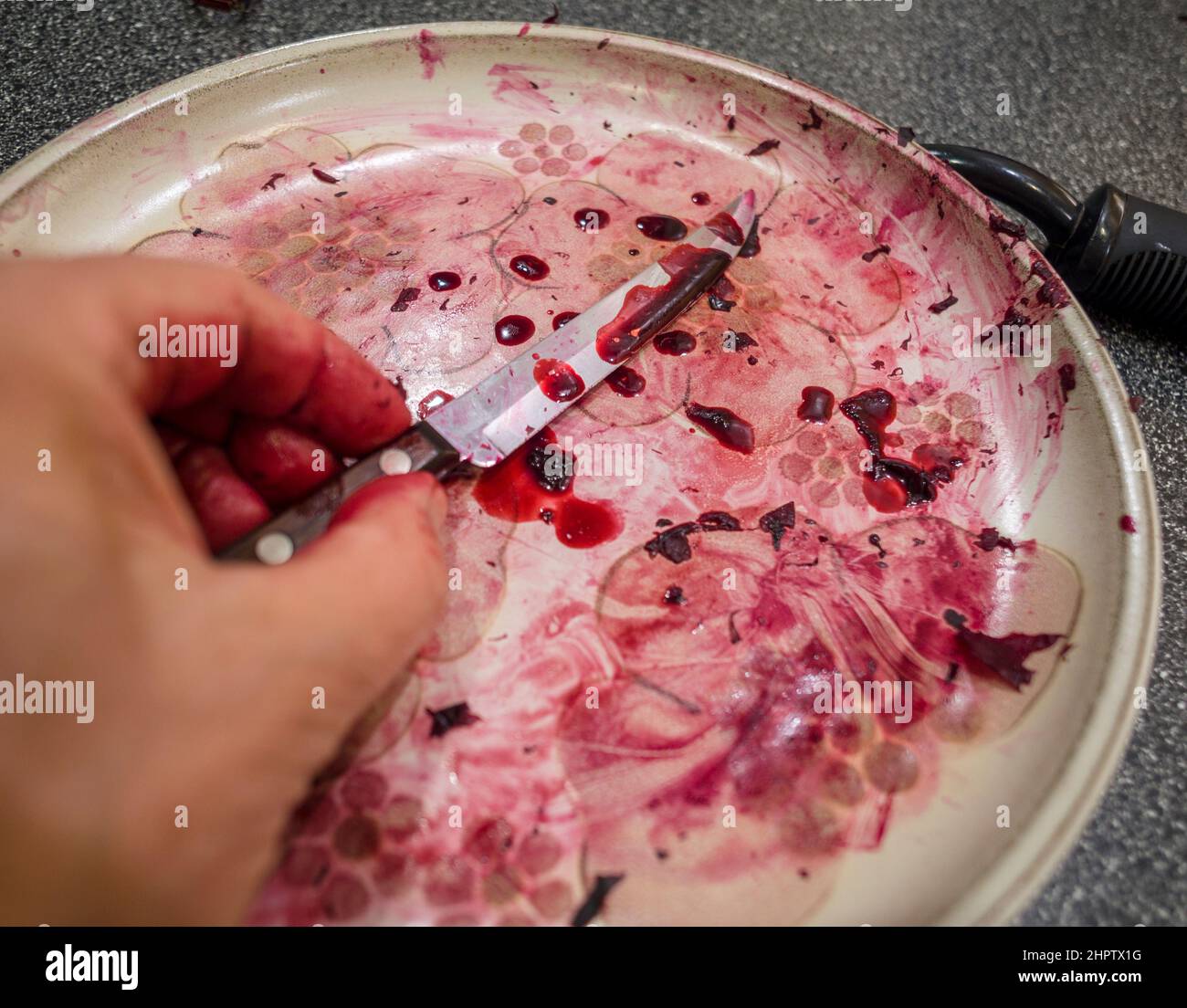 Succo di barbabietola e coltello da parare: Una mano raccoglie un coltello da parare ricoperto di succo di barbabietola rosso scuro che sembra un po' di sangue. Foto Stock
