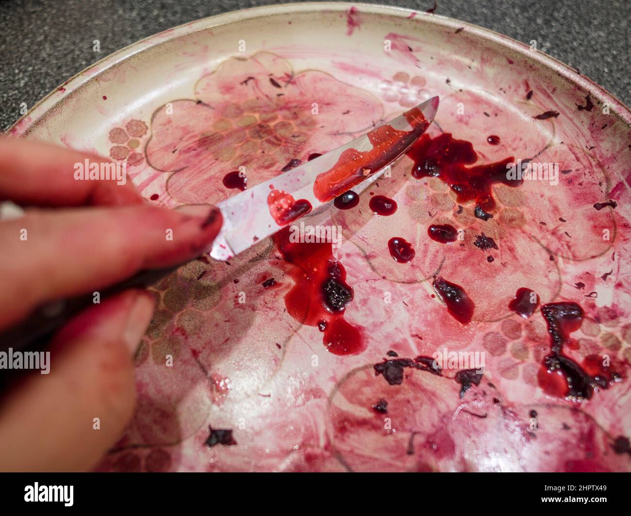 Succo di barbabietola e coltello da parare: Una mano raccoglie un coltello da parare ricoperto di succo di barbabietola rosso scuro che sembra un po' di sangue. Foto Stock