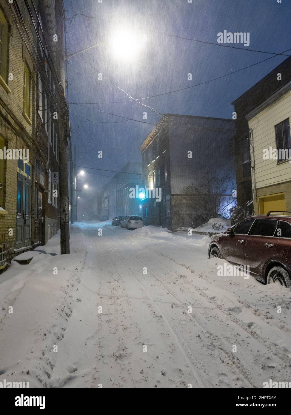 Tempesta di neve serale a Quebec City: La neve gira intorno a una stretta luce su una stretta strada di Quebec City. La strada si riempie rapidamente di neve e le auto parcheggiate sono innevate. Foto Stock