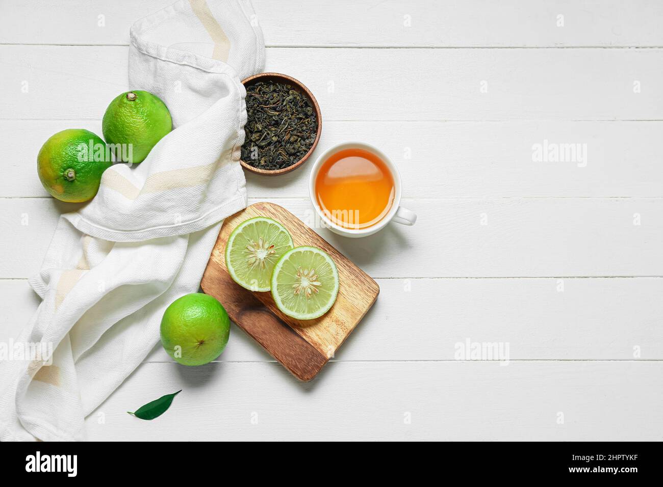 Composizione con tazza di tè, foglie secche e frutti di bergamotto maturi su sfondo bianco di legno Foto Stock
