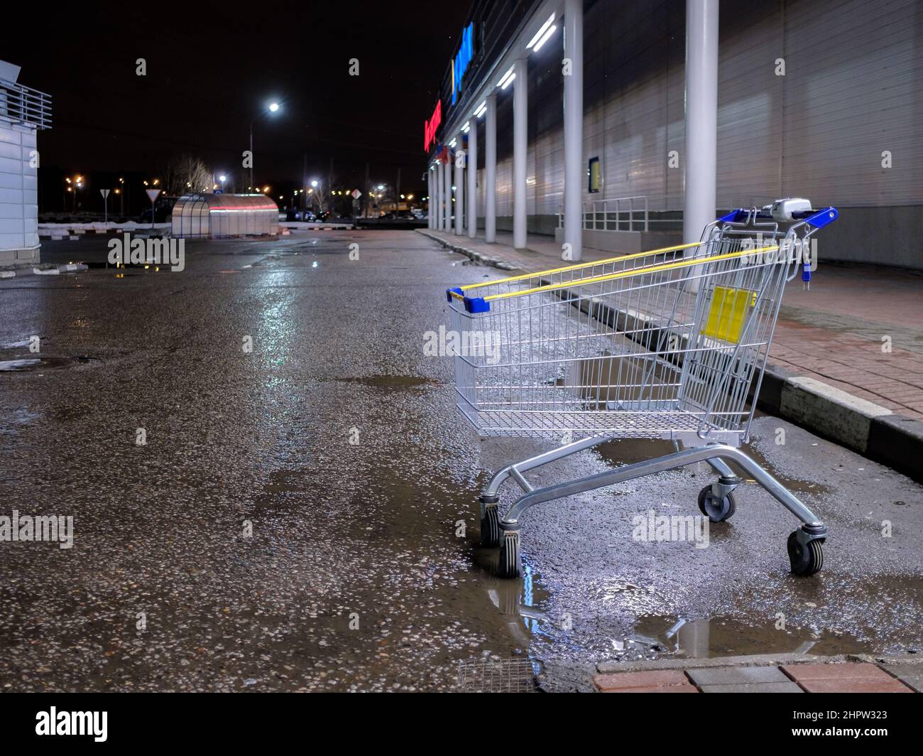 Un carrello di metallo da un supermercato in un parcheggio notturno. Messa a fuoco selettiva. Un carrello vuoto al buio in un parcheggio del negozio. Foto Stock