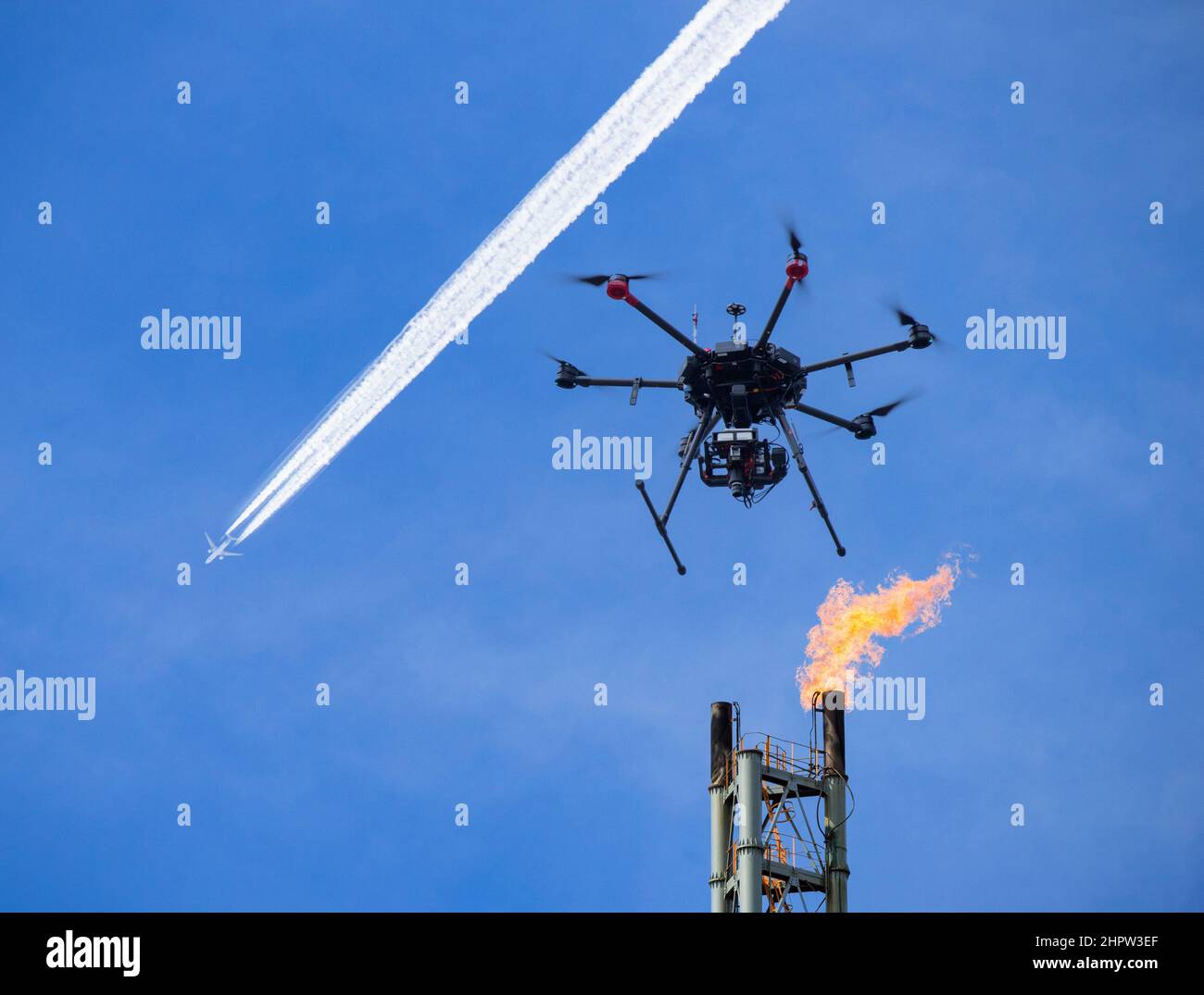 Drone che vola sopra la raffineria con pila di gas e aereo che vola sopra la testa. Foto Stock
