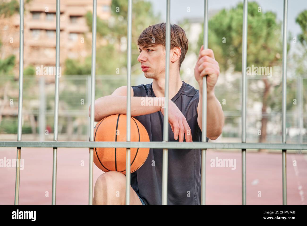 giocatore di basket in abbigliamento sportivo appoggiato sulla recinzione del campo Foto Stock