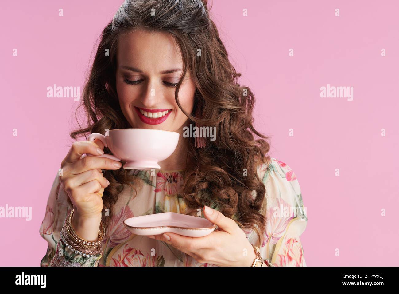 donna elegante felice in abito floreale con tazza di tè su sfondo rosa. Foto Stock