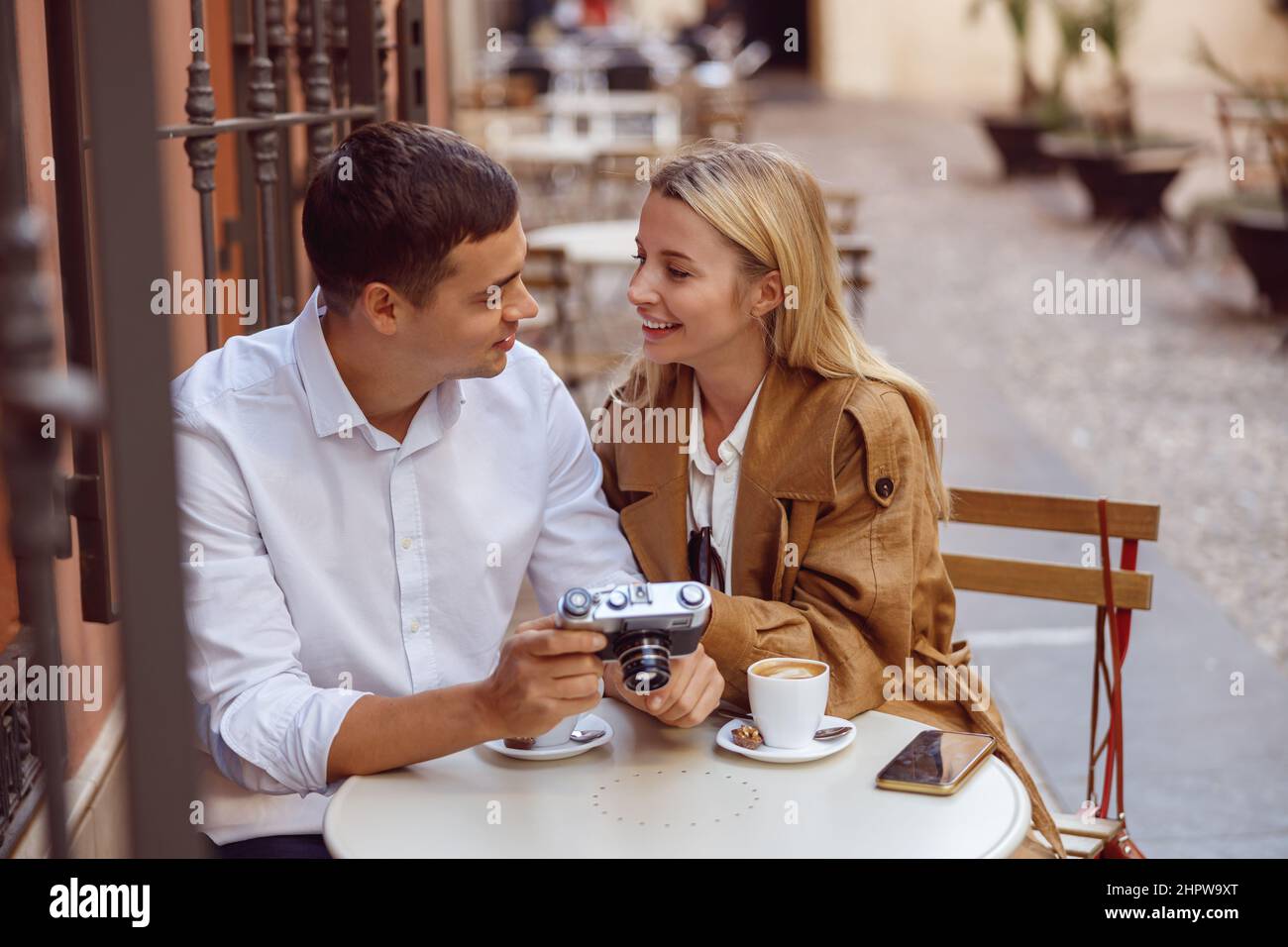 Donna sorridente seduta al tavolo del caffè di strada con un bell'uomo e rivedere le foto Foto Stock