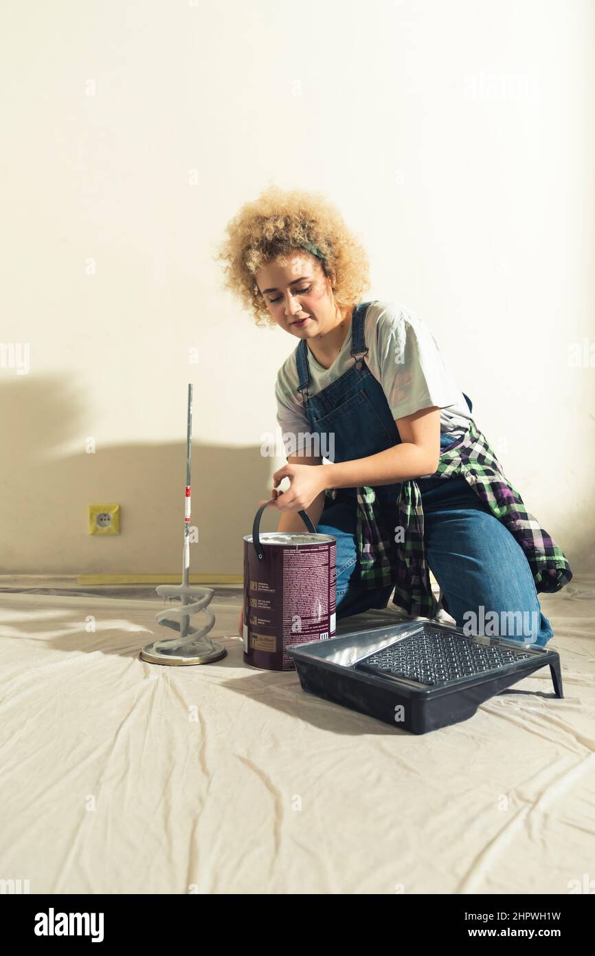 Capelli ricci ragazza caucasica in dungaree versando la vernice sul vassoio di vernice Foto di alta qualità Foto Stock