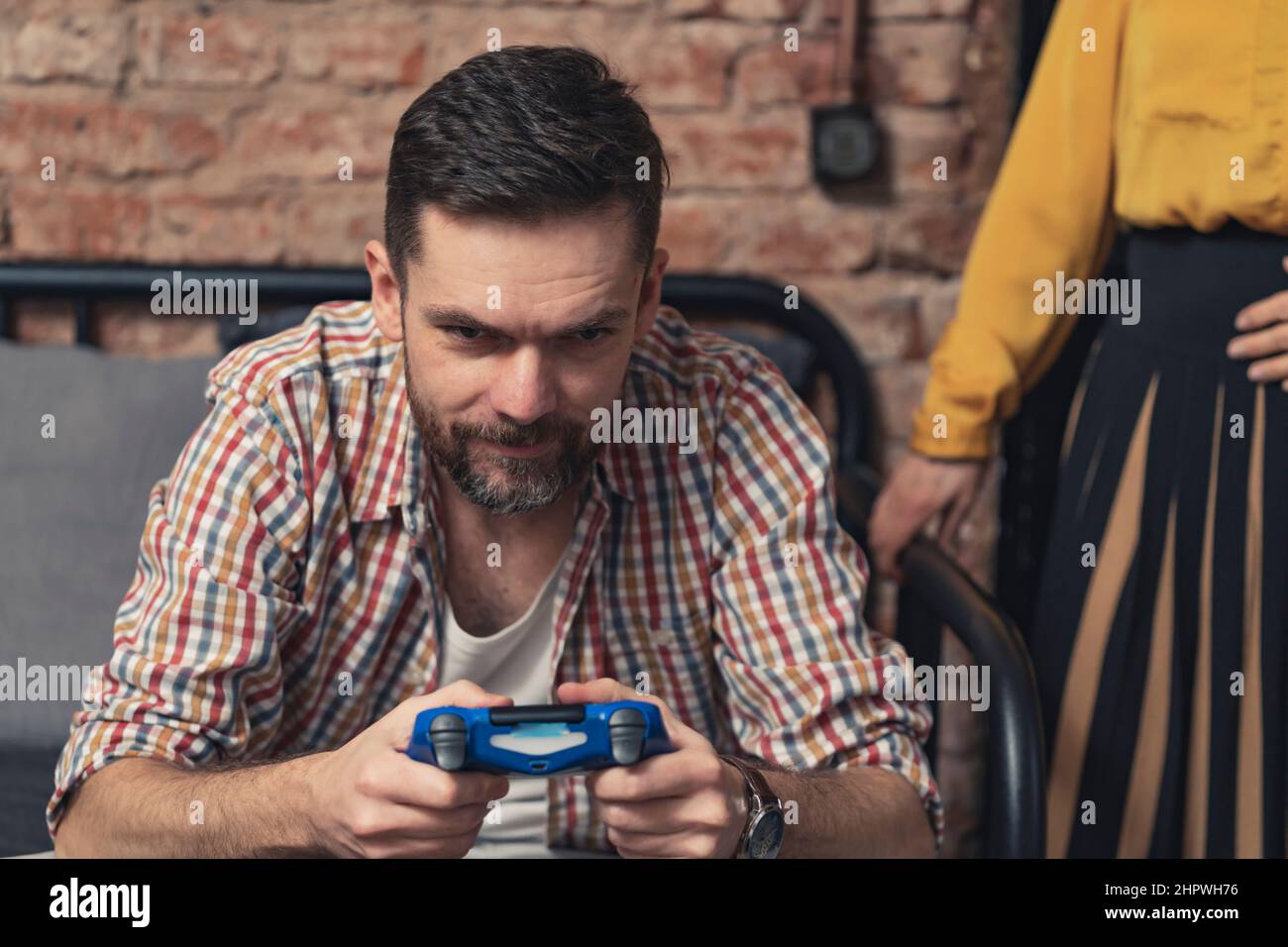 l'uomo caucasico in una maglietta senza bottoni che gioca con il controller di gioco blu e ignora la sua amica donna. Foto di alta qualità Foto Stock