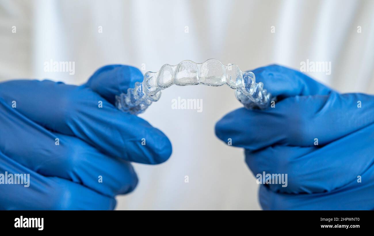 Mano maschio in guanti che tengono fermo allineatore dentale su sfondo bianco della clinica dentale per un bel trattamento dei denti. Diritto ortodontico rimovibile Foto Stock