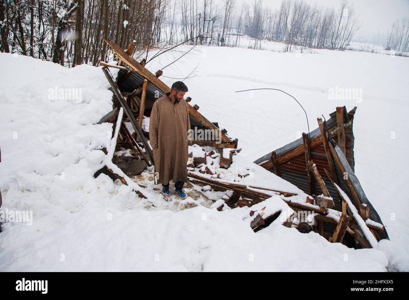 Budgam, India. 22nd Feb 2022. Un proprietario di casa ispeziona la sua casa danneggiata in un villaggio nella zona di Bugam Chadoora. La valle del Kashmir ha ricevuto pesanti nevicate che hanno portato alla chiusura di strade in zone lontane oltre al ritardo di diversi voli che operavano dall'aeroporto di Srinagar. Anche i servizi ferroviari locali sono stati sospesi. (Foto di Faisal Bashir/SOPA Images/Sipa USA) Credit: Sipa USA/Alamy Live News Foto Stock