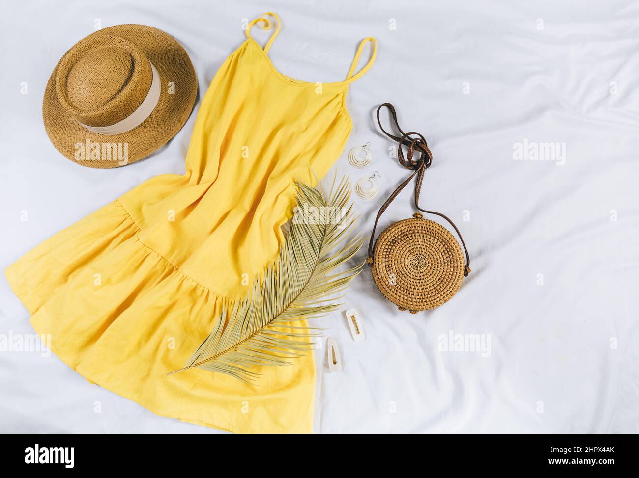 Cappello di paglia, abito giallo, borsa di paglia su sfondo bianco. Outfit estivo alla moda. Stay piatto con vestiti per vacanze e vacanze. Foto Stock