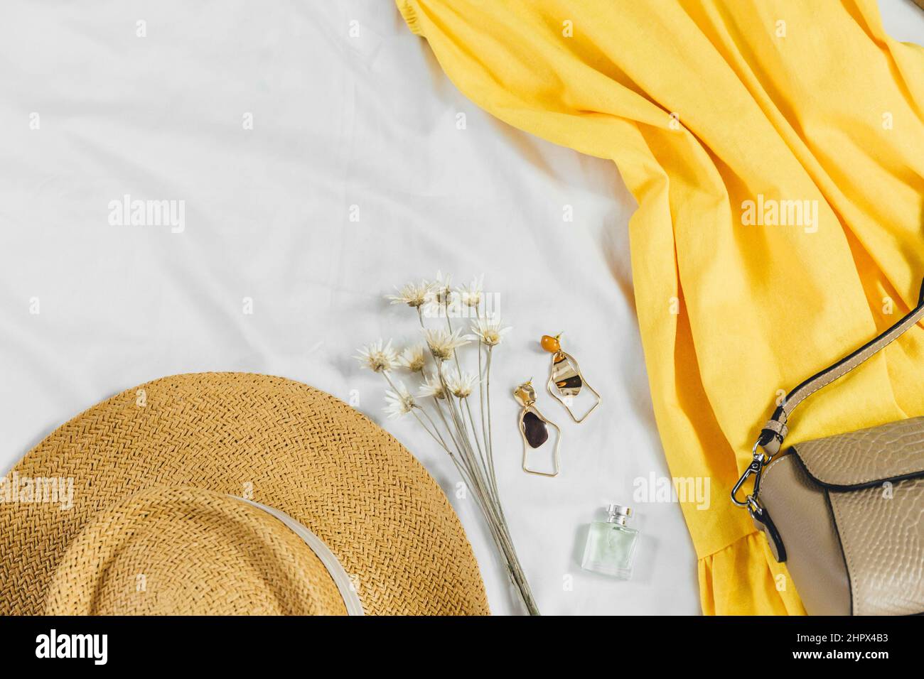 Cappello di paglia, abito giallo, borsa di paglia su sfondo bianco. Outfit estivo alla moda. Stay piatto con vestiti per vacanze e vacanze. Foto Stock