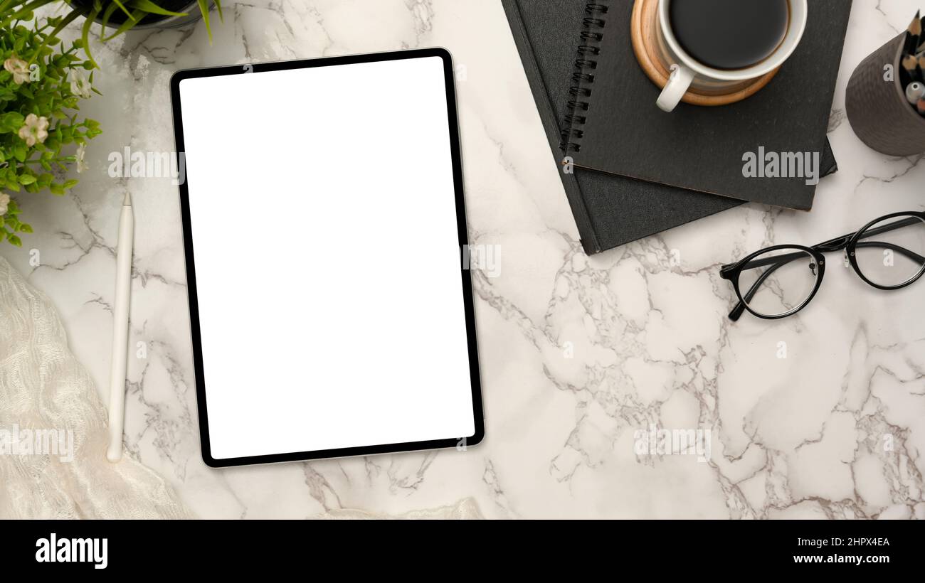Area di lavoro moderna con computer tablet portatile con schermo bianco e forniture per ufficio su sfondo bianco in marmo. Vista dall'alto Foto Stock