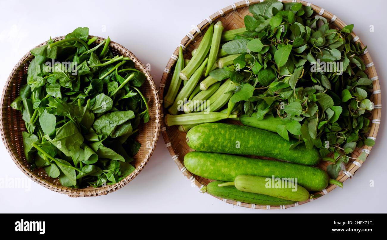 Verdure verdi appena raccolte dal giardino della città sulla casa sul tetto della città di ho chi Minh, frutta di melone, calabash, okra, spinaci sul cesto su sfondo bianco Foto Stock