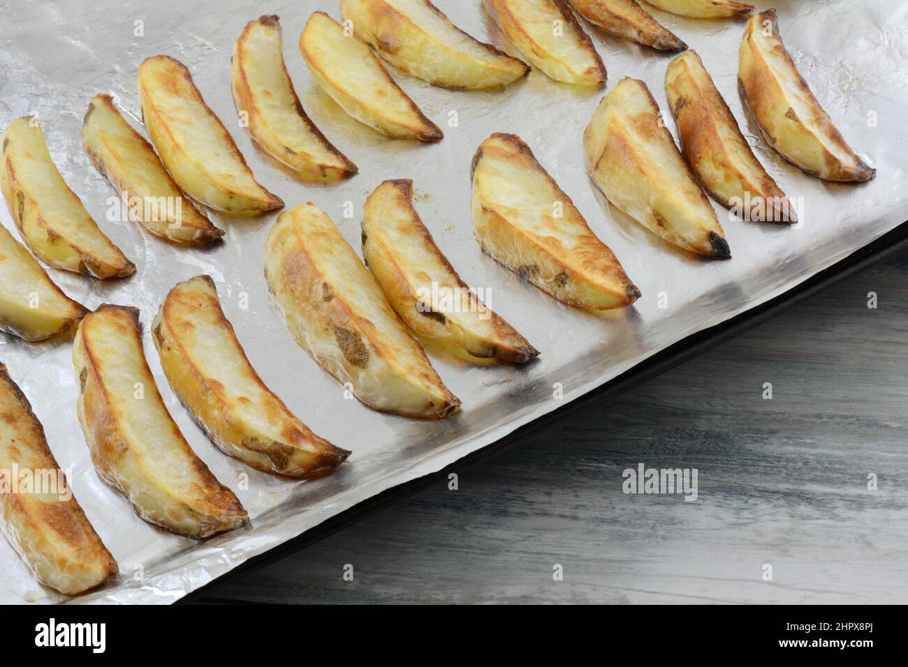 Spicchi di patate arrosto in file su foglio di alluminio su foglio da forno Foto Stock