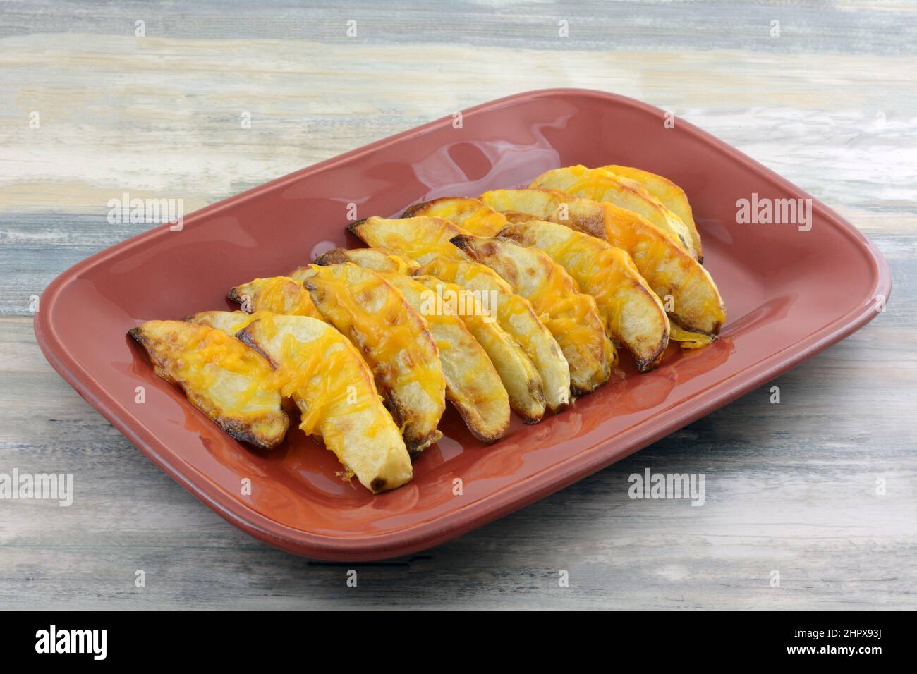 Spicchi di patate al forno con aggiunta di formaggio fuso grattugiato sul piatto da portata rosso Foto Stock