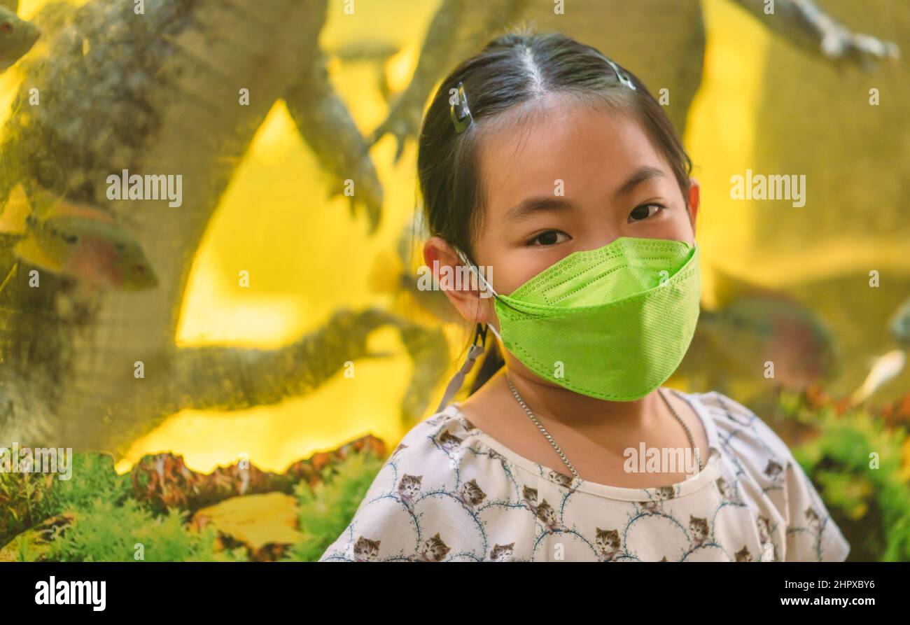 Ritratto di una ragazza asiatica felice in uno zoo della Thailandia, indossando una maschera per proteggere il virus, sfondo sfocato del coccodrillo in un serbatoio di vetro, bianco Foto Stock