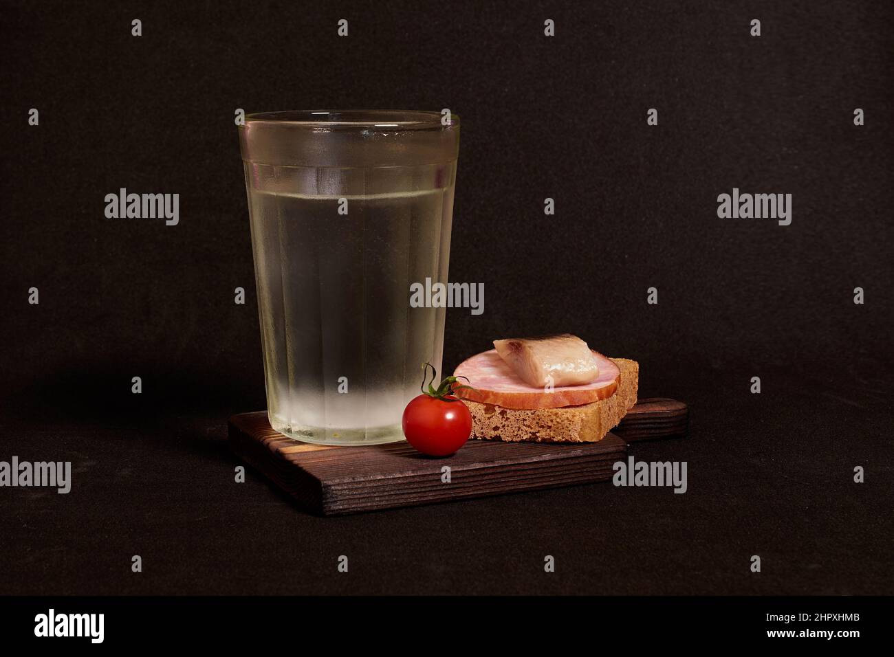 Bicchiere sfaccettato di vodka, panino con pane di segale, aringhe, prosciutto, pomodoro Foto Stock