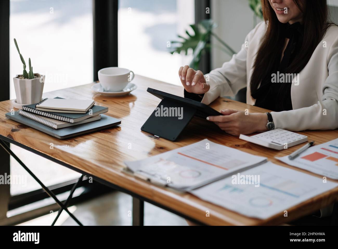 Primo piano di un grafico di analisi della mano di una donna asiatica d'affari su tablet digitali e calcolatrice del lavoro cartaceo sul posto di lavoro Foto Stock