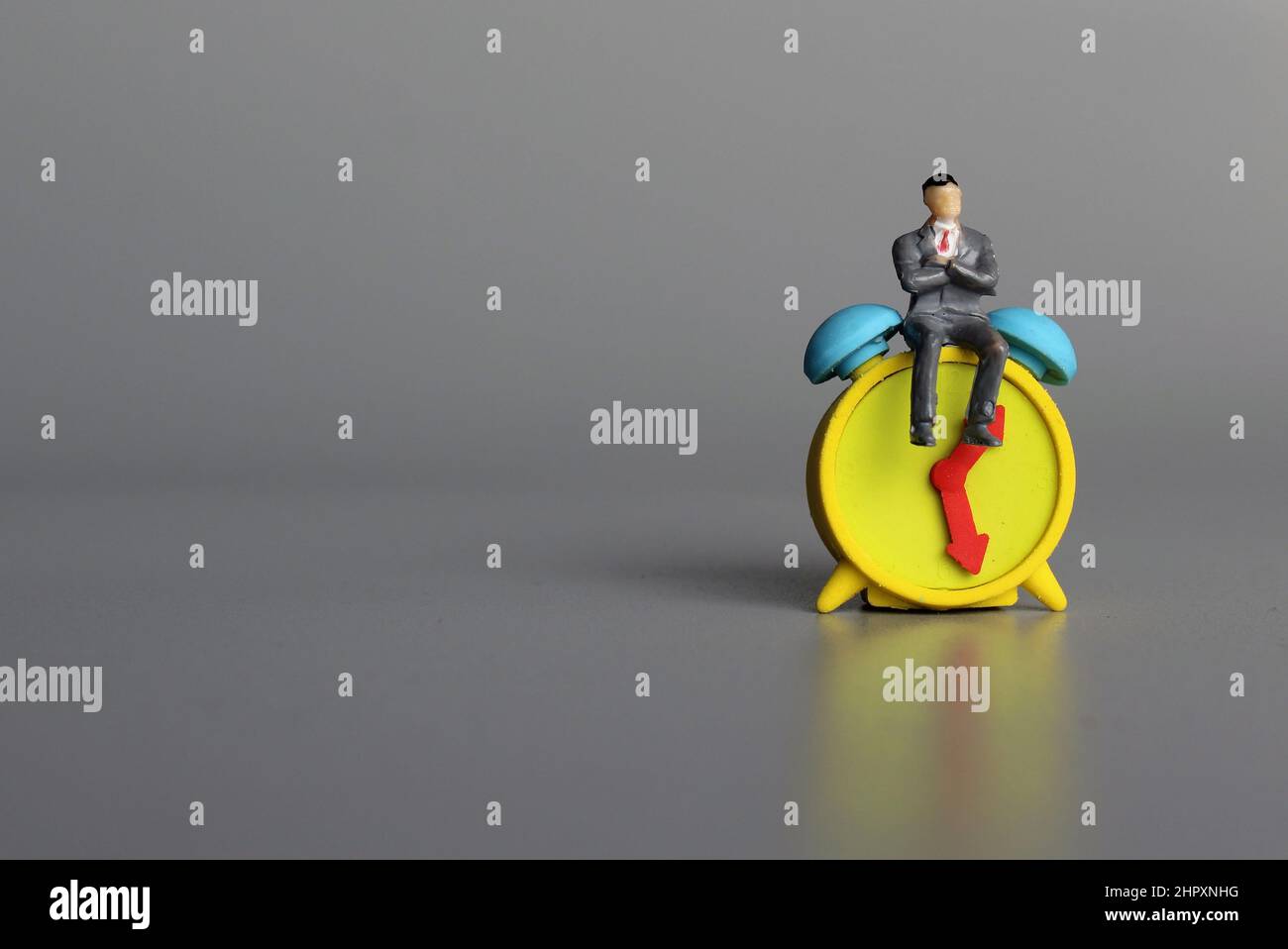 Concetto di gestione del tempo. Uomo seduto sopra la sveglia. Spazio di copia per il testo. Foto Stock