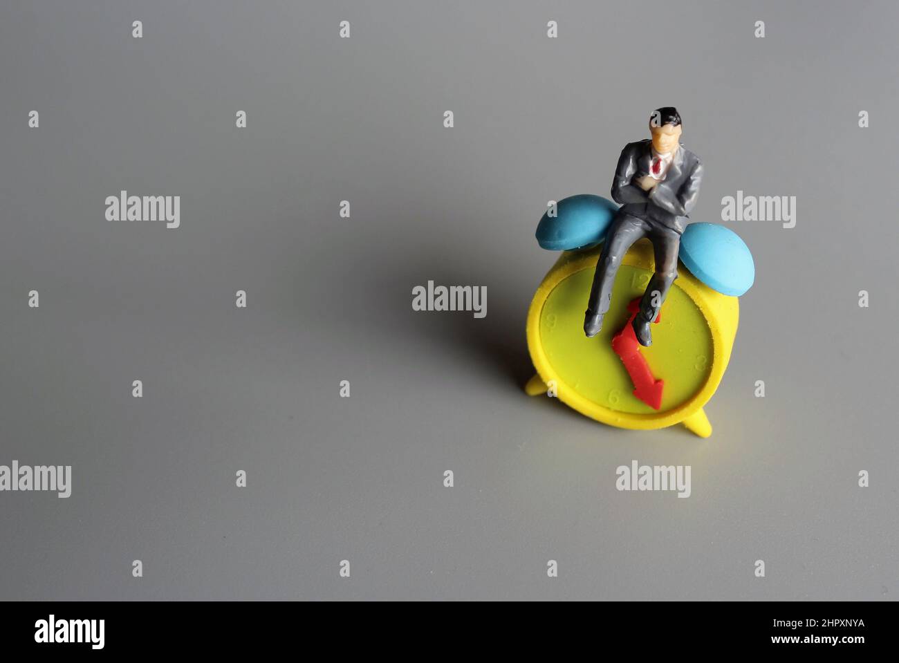 Concetto di gestione del tempo. Uomo seduto sopra la sveglia. Spazio di copia per il testo. Foto Stock