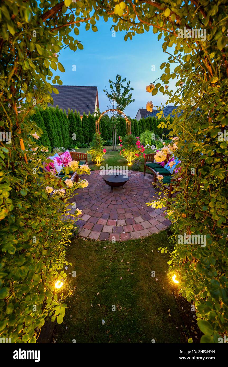 Bel giardino con cerchio di pietra e ciotola di fuoco nel buio della sera con lampade solari nel terreno Foto Stock