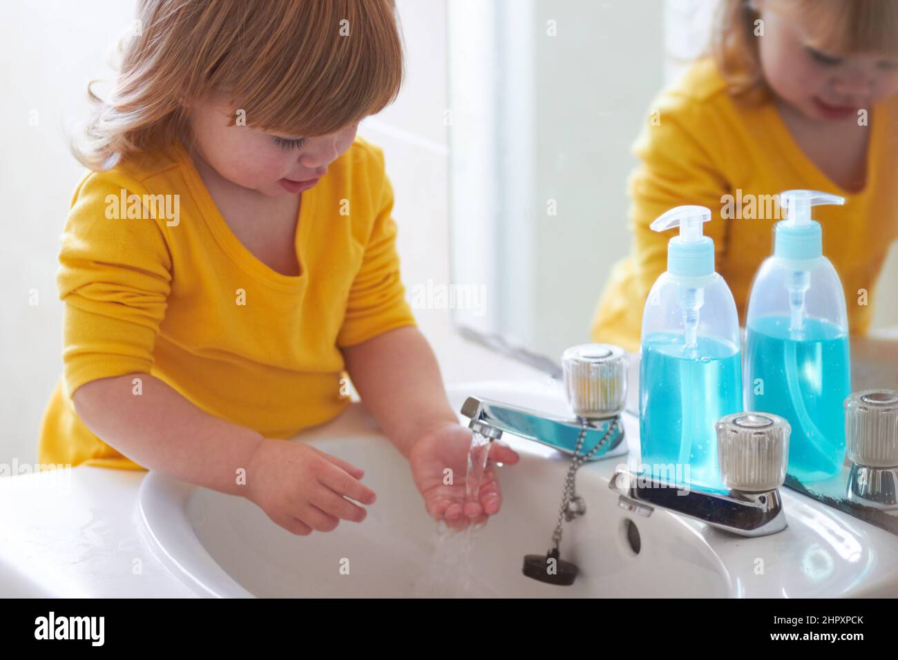 Guarda, il suo correre attraverso le mie dita. Una bambina adorabile che lava le mani in bagno. Foto Stock