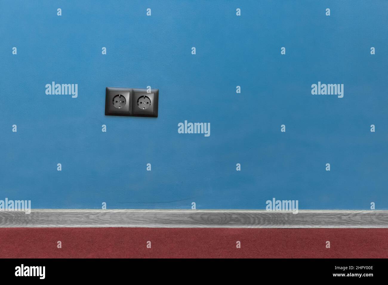 Doppia presa nera alimentazione casa energia fornire elettricità su sfondo blu parete e battiscopa pavimento baseboard materiale pavimento. Foto Stock