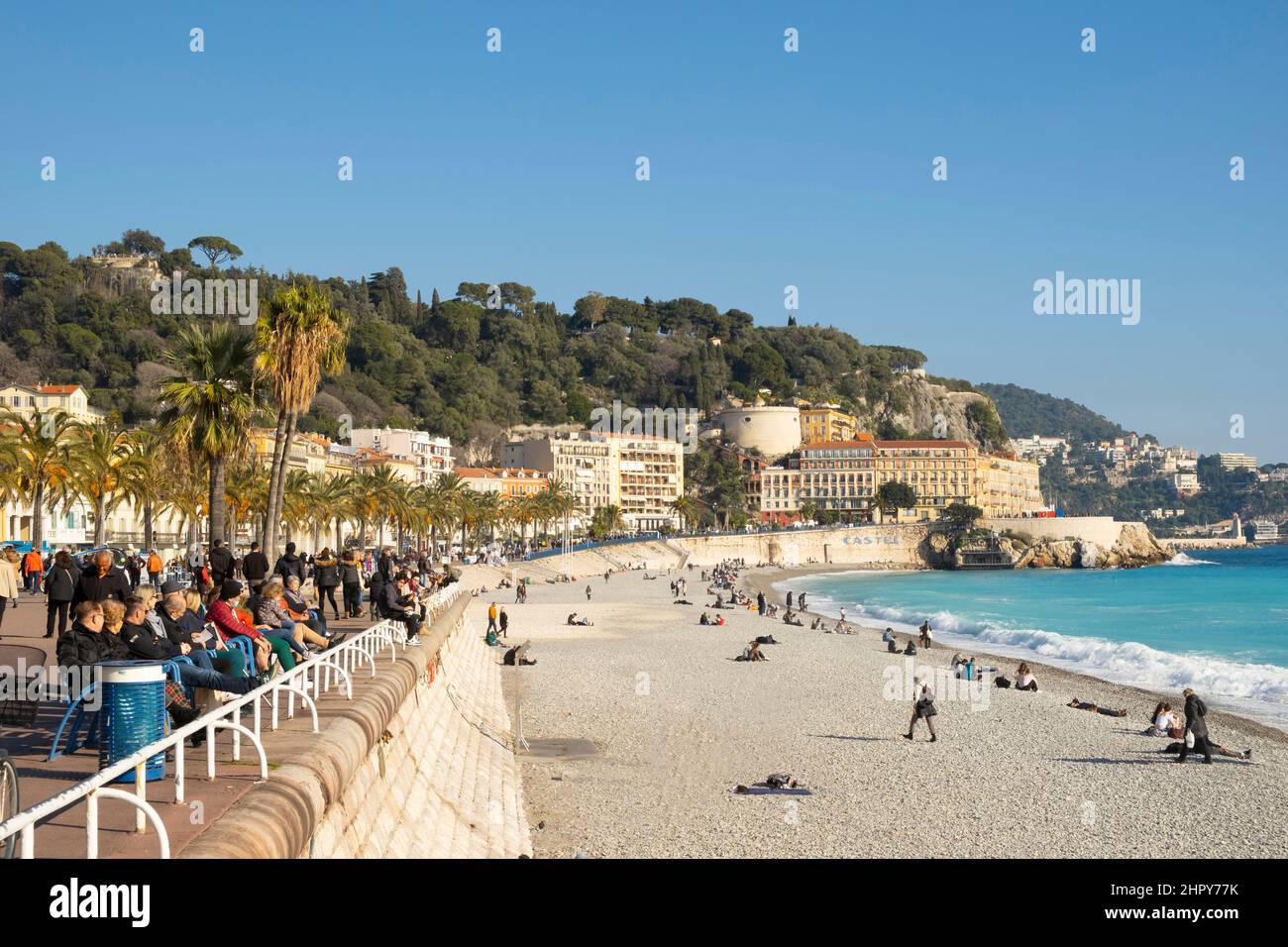 Persone sedute su panchine lungo la Promenade des Anglais e sulla spiaggia di Nizza in inverno. Costa Azzurra, Francia Foto Stock