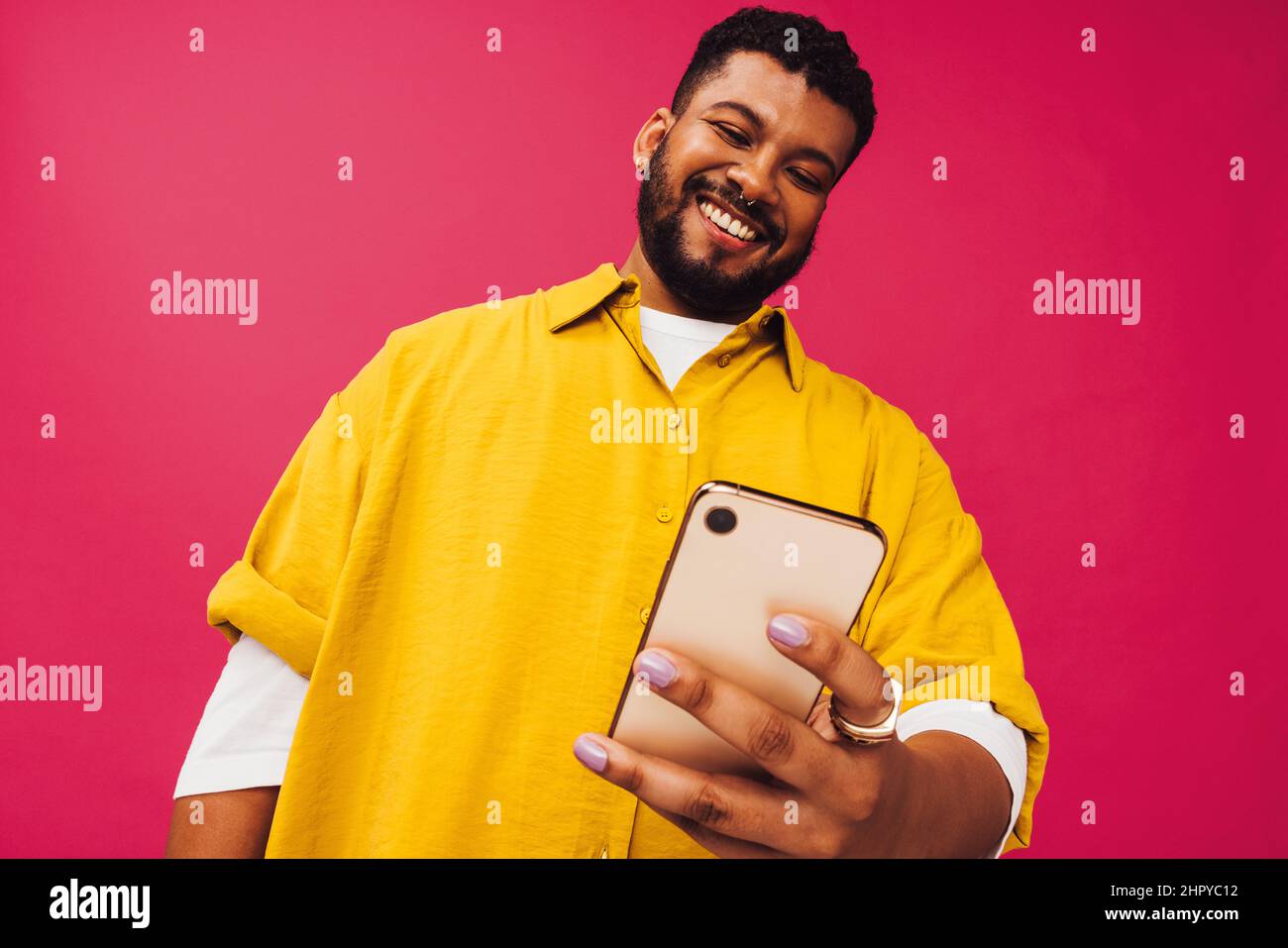 Navigare in rete in studio. Felice uomo giovane sorridente allegro mentre si usa uno smartphone per navigare in Internet. Spensierato giovane uomo in piedi da solo a Foto Stock