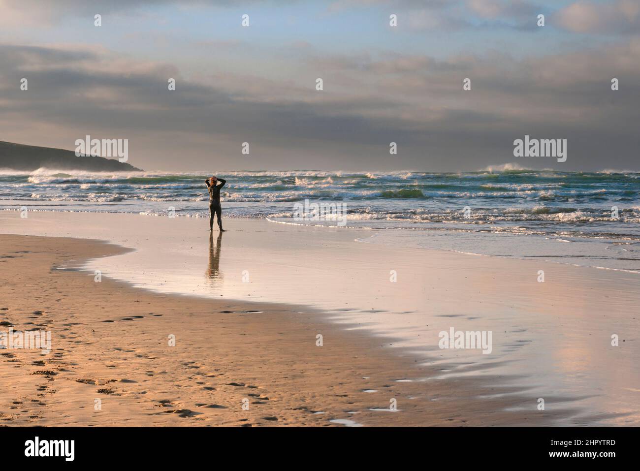 Un uomo che indossa un costume da bagno in piedi sulla riva e guarda verso il mare a Crantock Beach a Newquay in Cornovaglia. Foto Stock