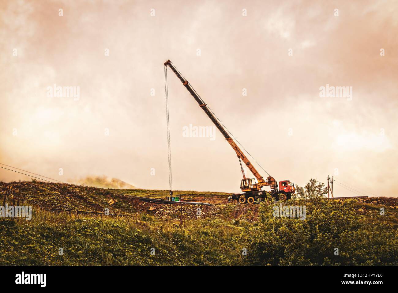 2019 07 18 Stepantsminda Georgia - Tall gru e trattore in cantiere su una sporgenza con nebbia e barey montagna visibile sullo sfondo nel Caucaso Foto Stock