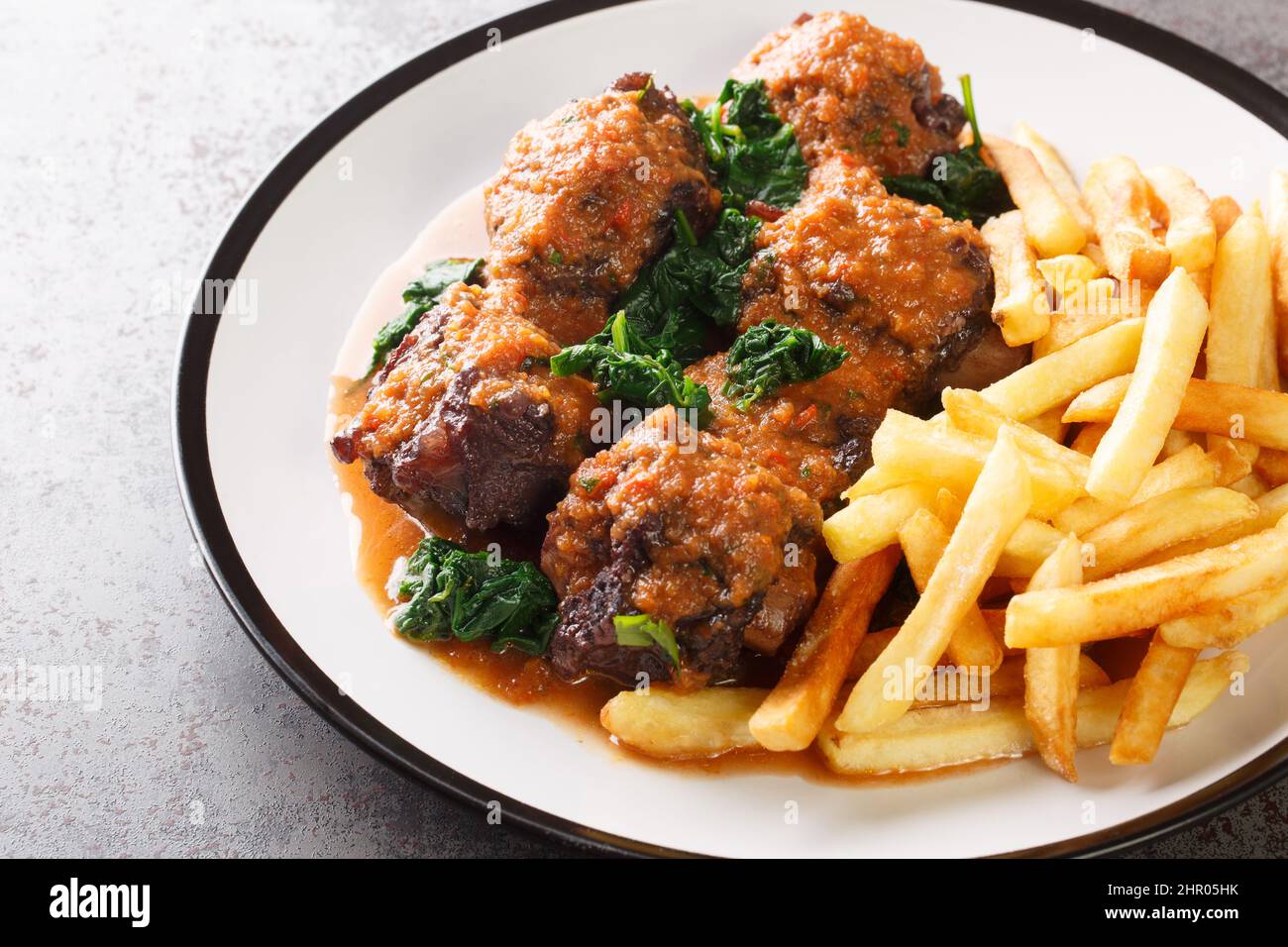 Gustoso Rabo de toro o stufato di coda di bue servito con patatine fritte su piatto bianco sul tavolo di cemento. Orizzontale Foto Stock