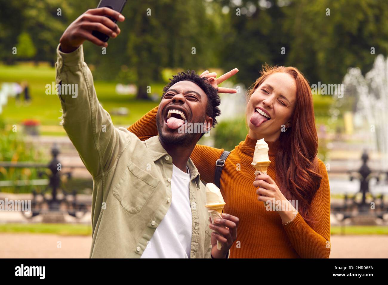 Giovane coppia che viaggia attraverso la città insieme mangiando gelati in Park e prendendo Selfie Foto Stock